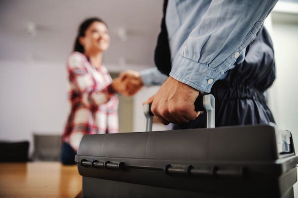 Un électricien avec sa caisse à outils sert la main de sa cliente