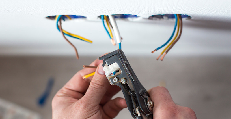 un électricien à domicile qui dénude les fils électrique d'un interrupteur