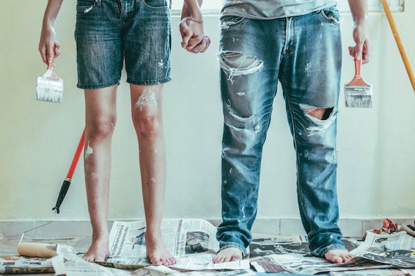 Deux personnes avec un pinceau dans la main et des tâches de peinture partout sur leurs vêtements