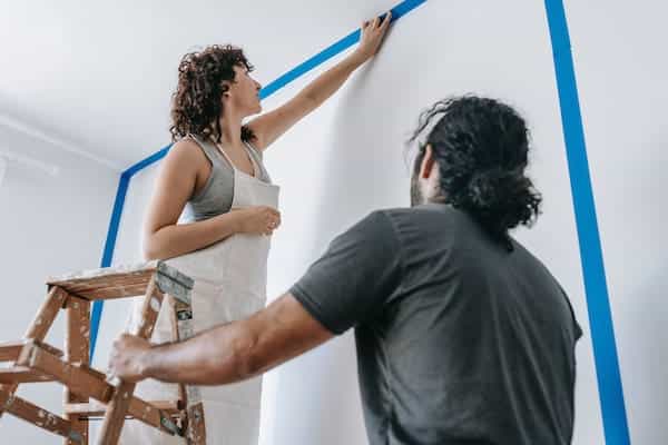 Un couple qui prépare le mur en recouvrant avec du ruban adhésif les angles des murs